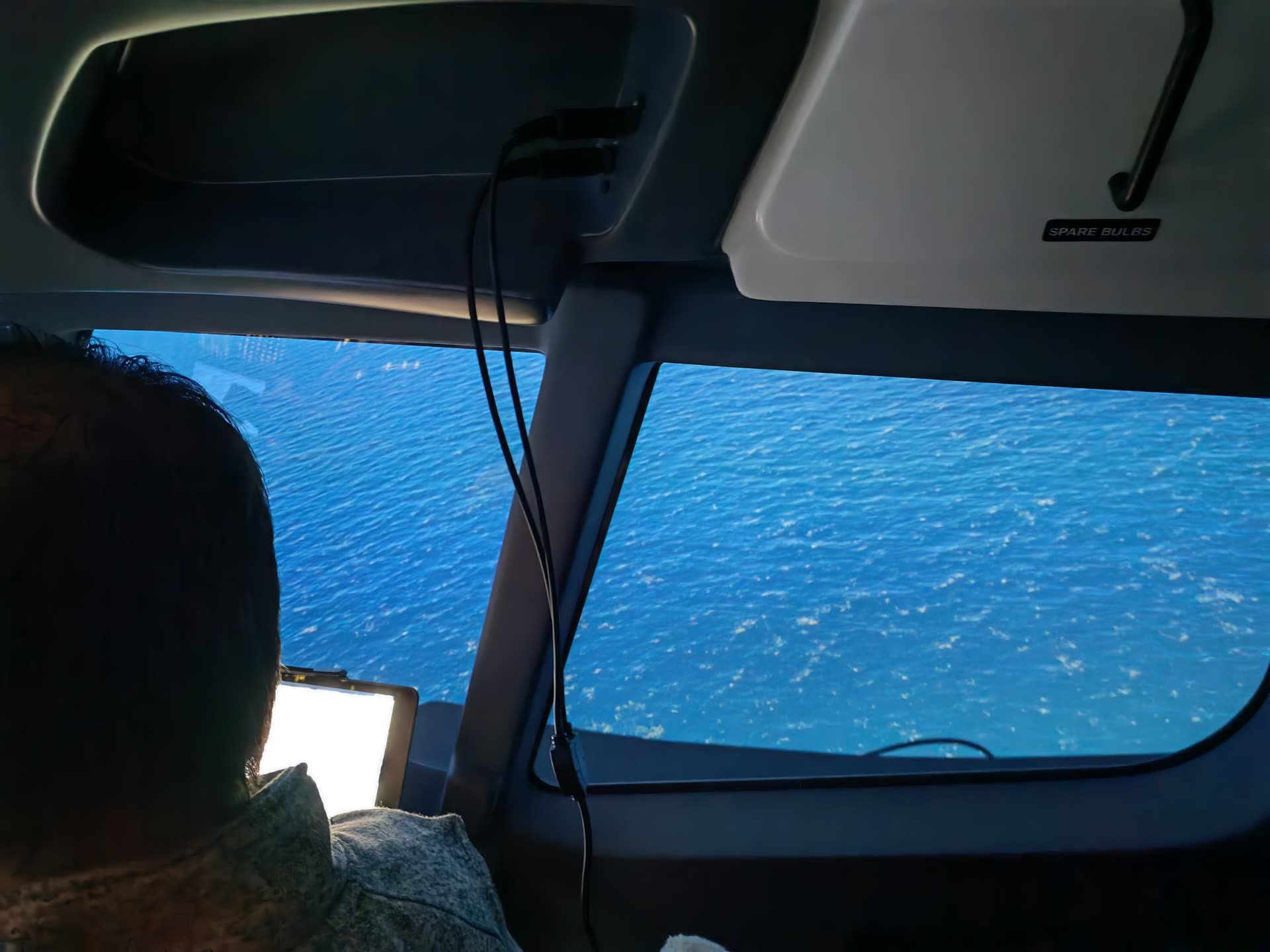Over-shoulder view through the captain's side window, deep blue ocean visible below